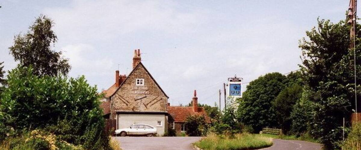 A rural road with a white car parked in front of a stone building with a garage.