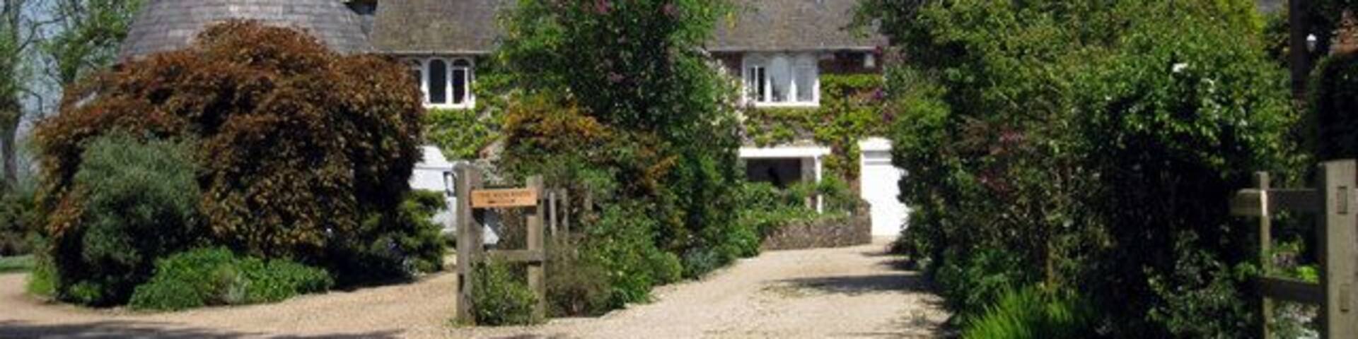 A rural setting with traditional conical-roofed buildings, a gravel path, and lush greenery.