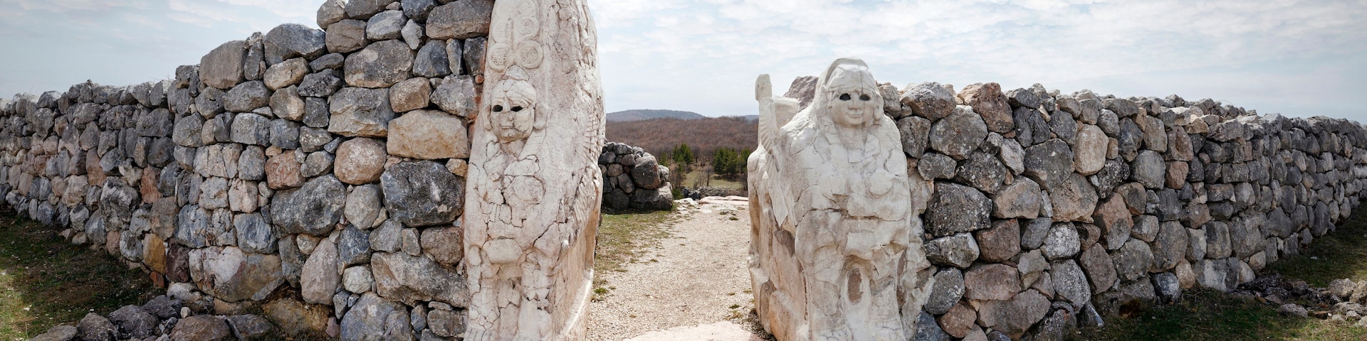 Un muro de piedra con figuras labradas y un sendero estrecho que lo atraviesa.