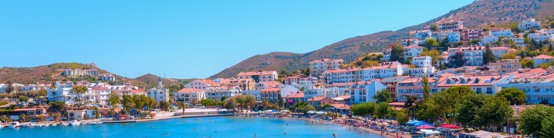 A coastal town with a clear blue sea, colorful buildings, and a hilly backdrop.
