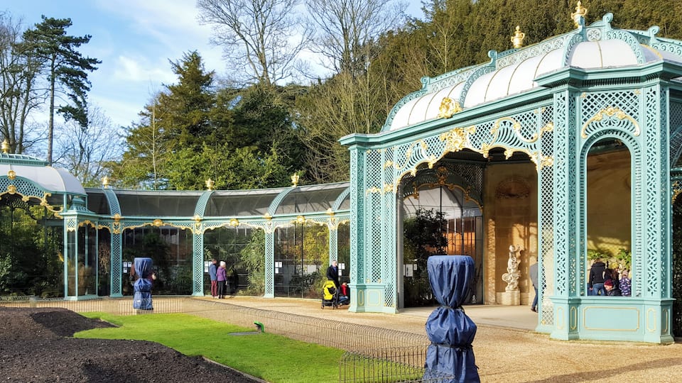 Ornate glasshouse structures with intricate metalwork and a well-maintained garden.
