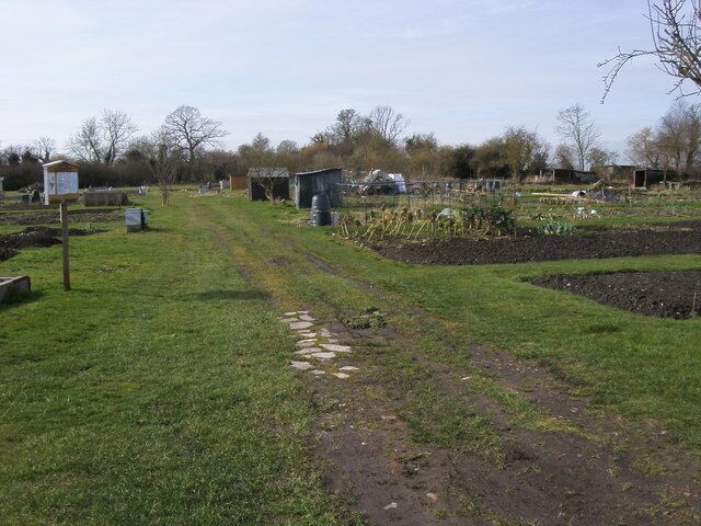 A rural landscape with a dirt path, green fields, and farm buildings.