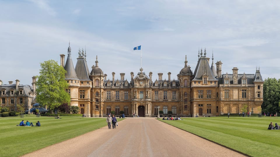A grand historic building with ornate architecture, a large lawn, and a flag flying atop.