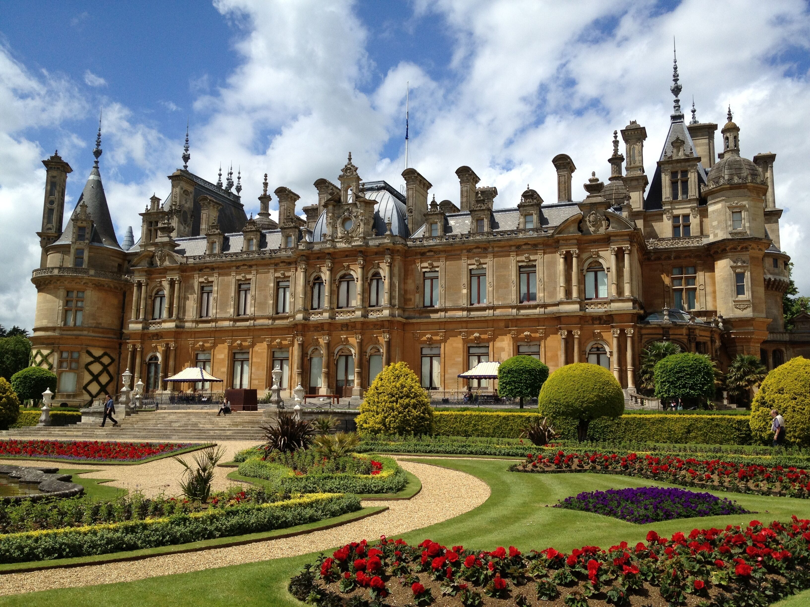 A grand historic building with ornate architecture, a well-manicured garden, and a clear blue sky.