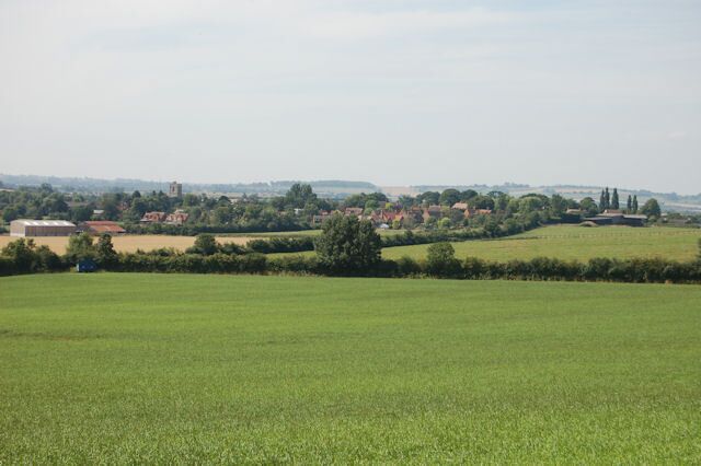 A rural landscape with green fields, scattered trees, and distant buildings.