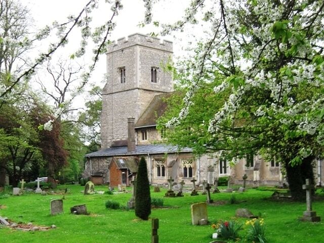 A church with a tower, surrounded by a cemetery with gravestones and blooming trees.