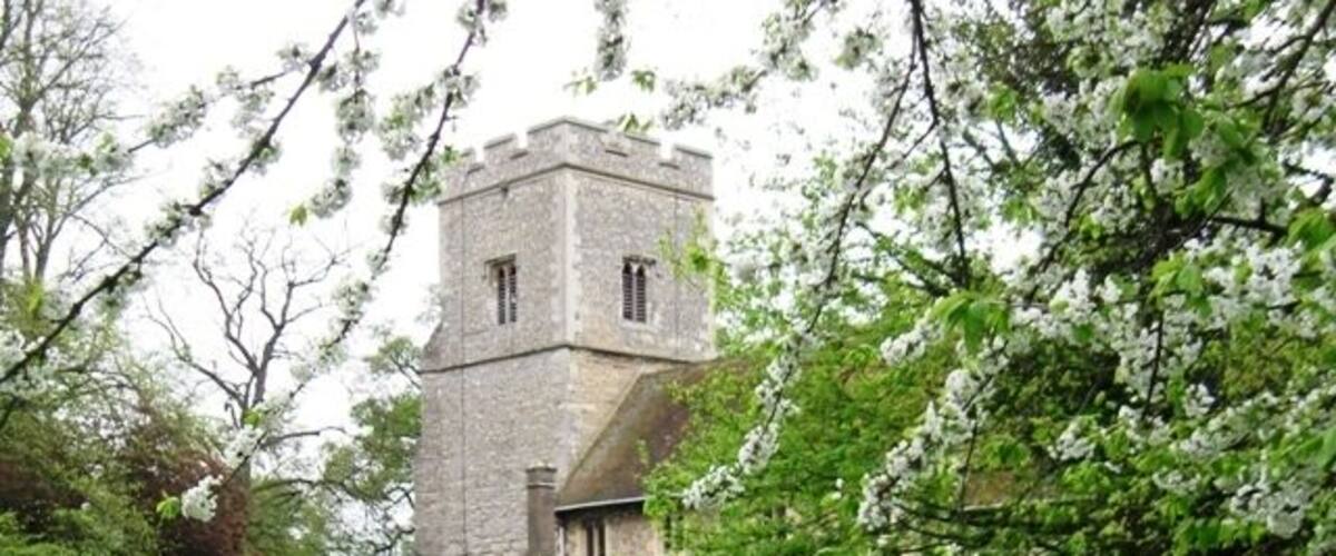 A church with a tower, surrounded by a cemetery with gravestones and blooming trees.