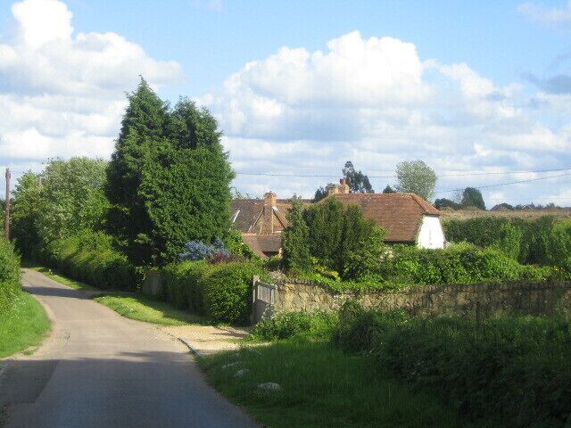 A narrow rural road flanked by lush greenery and traditional houses.