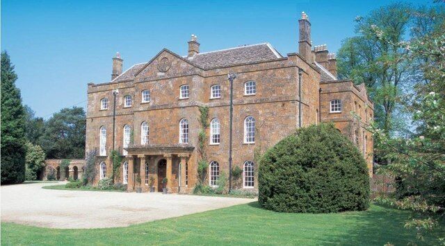 A large, historic stone building with multiple windows and a well-maintained lawn.