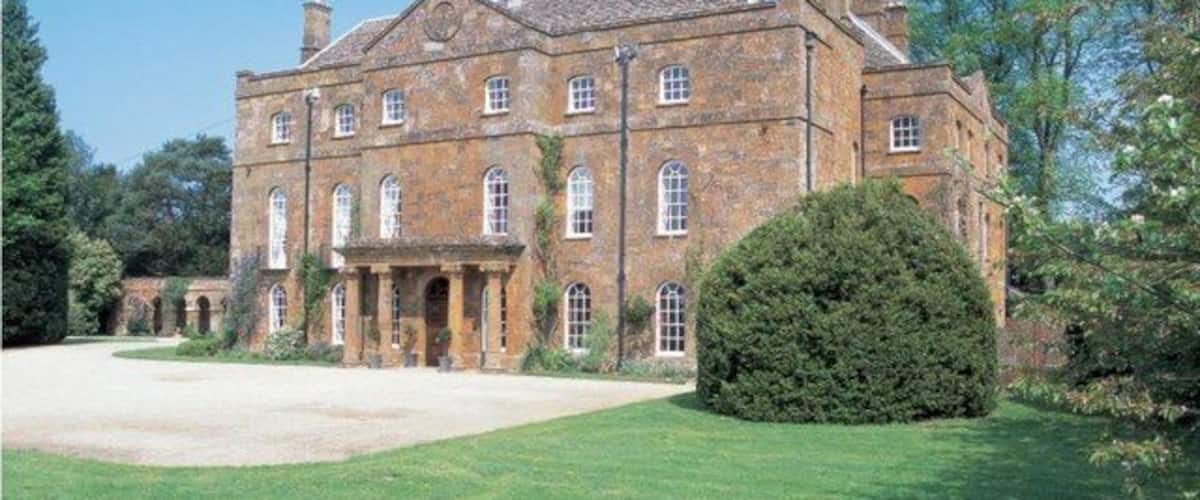 A large, historic stone building with multiple windows and a well-maintained lawn.