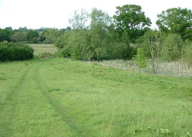 Jurassic Way long distance trail. The pond is on the right, Jurassic Way climbs a field to a railway bridge