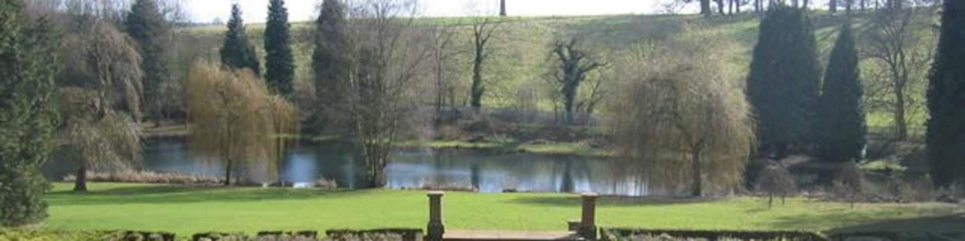 Wroxton Abbey grounds. The gardens of 553107, looking the other way from 553109. In the middle years of the eighteenth century Lancelot Brown remodelled the gardens making use woodland and water in his characteristic personal style. The classic features included a lawn sweeping up to the house, clumps of trees, a serpentine lake and an encircling tree belt and carriage drive, also showing a serpentine geometry. This is the style of what is often known as the 'English landscape garden', or possibly even the 'Brownian' style.