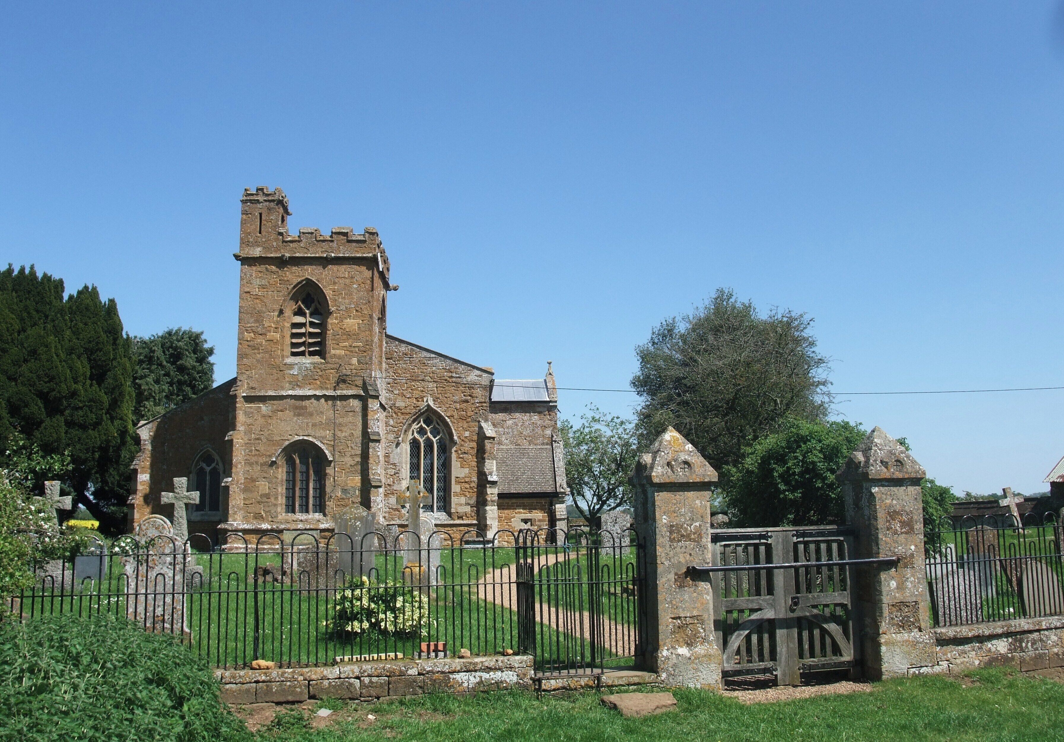 A historic church with a tall tower and arched windows, surrounded by a cemetery and a metal fence.