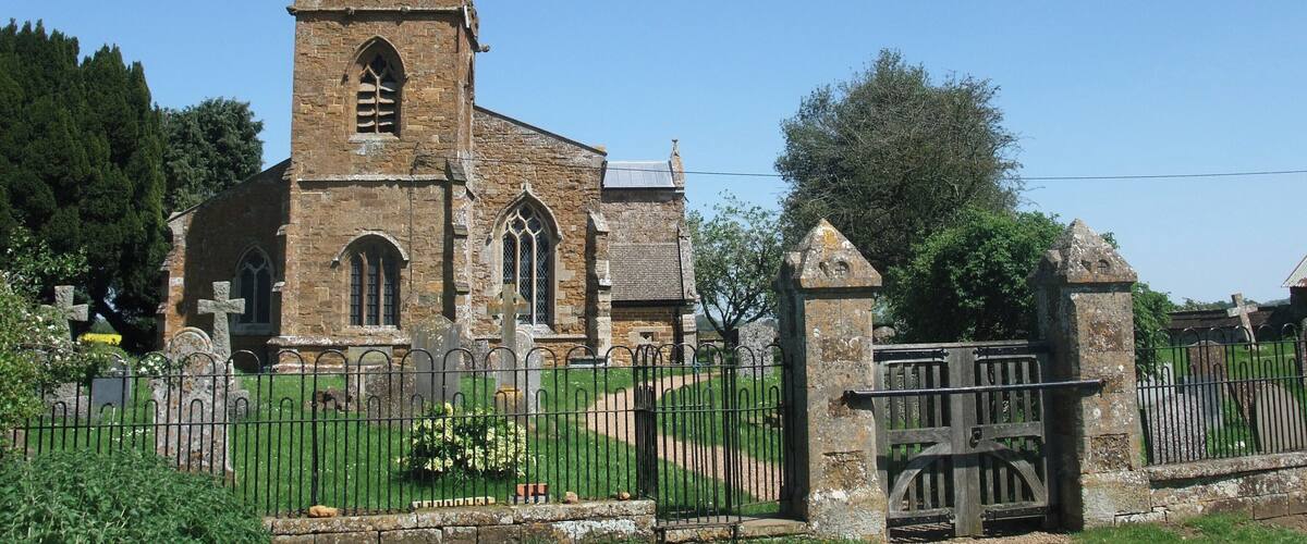 A historic church with a tall tower and arched windows, surrounded by a cemetery and a metal fence.