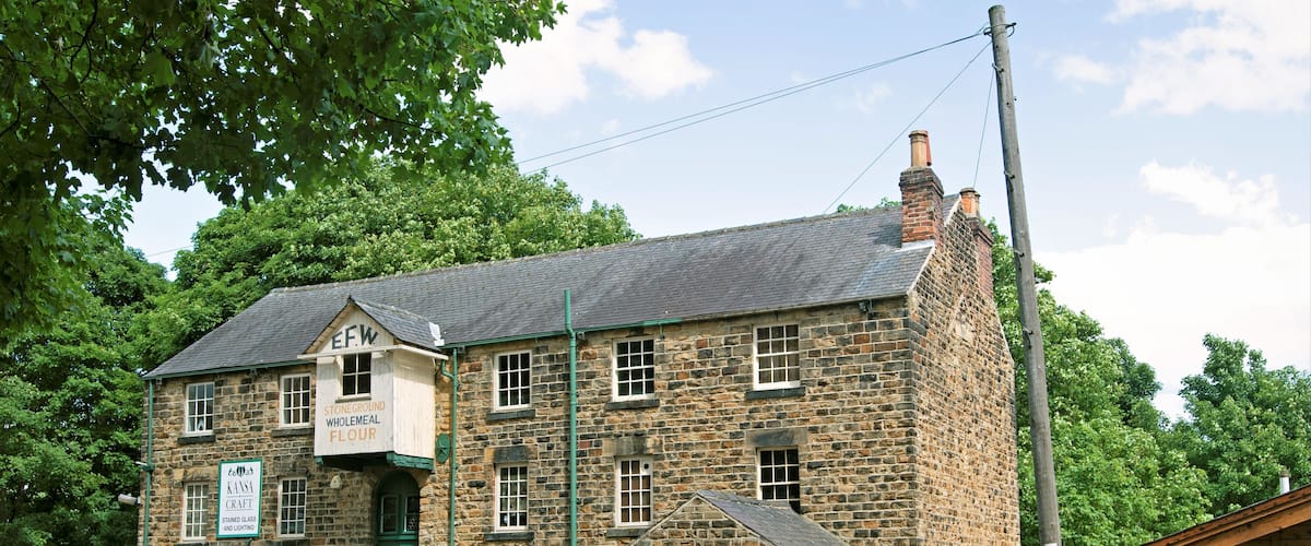 Un edificio de piedra con una puerta verde y ventanas, con el letrero 'EFW Stoneground Wholemeal Flour'.