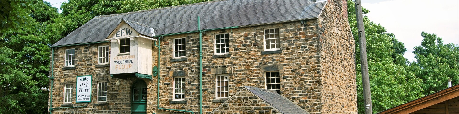 Um edifício de pedra com porta e janelas verdes, com a inscrição 'EFW Stoneground Wholemeal Flour'.