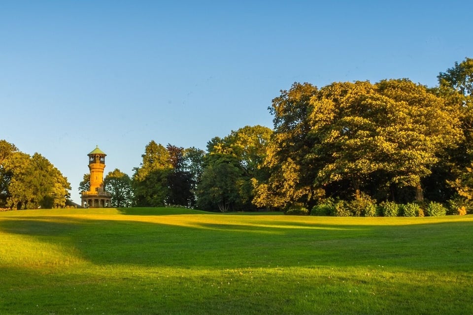 A lighthouse on a grassy hill with dense trees in the background.