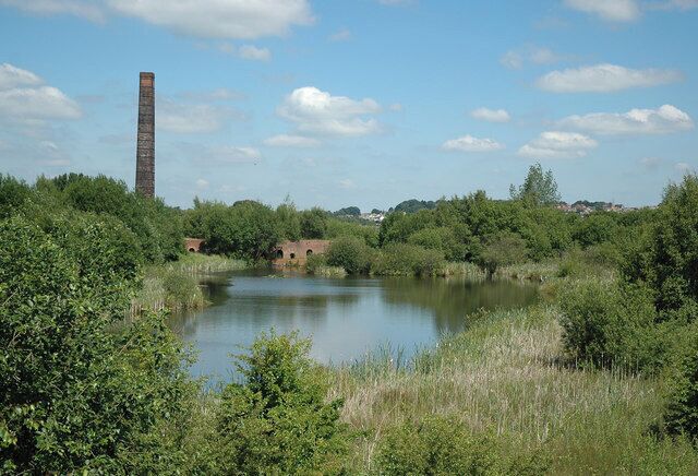 A river with a brick building and a tall chimney in the background.