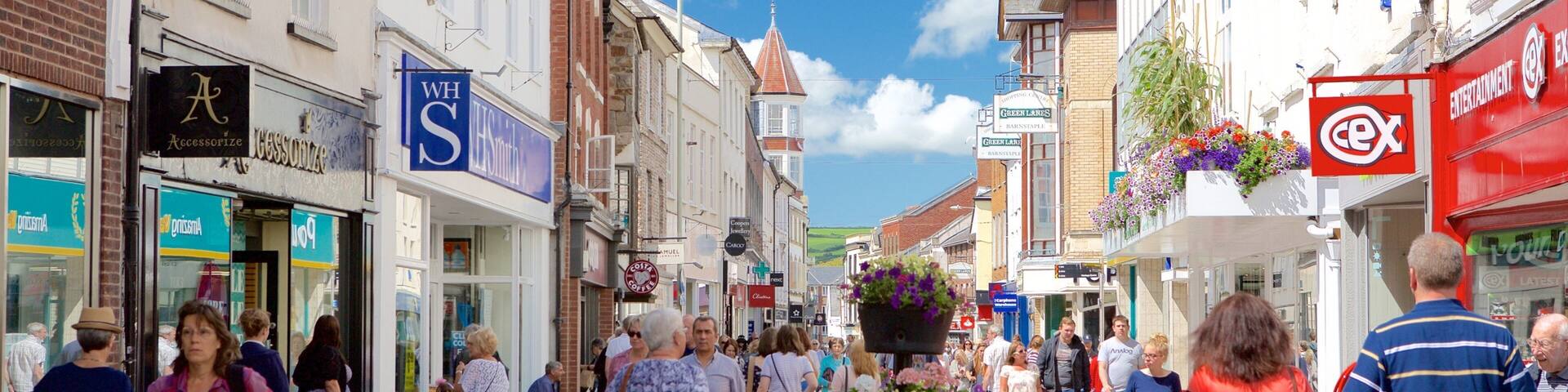 A busy pedestrian street lined with shops and cafes, with people walking and a dog on a leash.