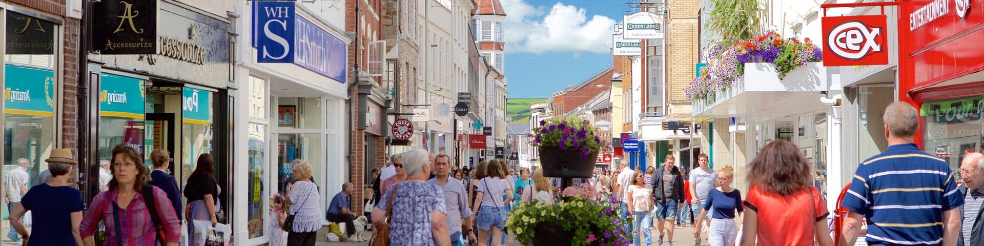 A busy pedestrian street lined with shops and cafes, with people walking and a dog on a leash.