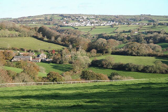 A rural landscape with rolling hills, a small village, and a prominent building in the foreground.