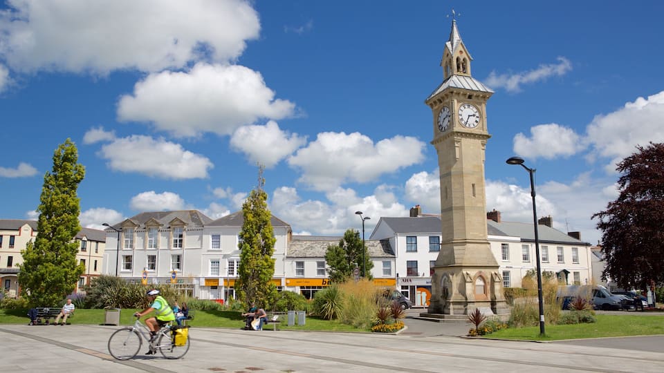 A town square with a clock tower, buildings, and a cyclist.