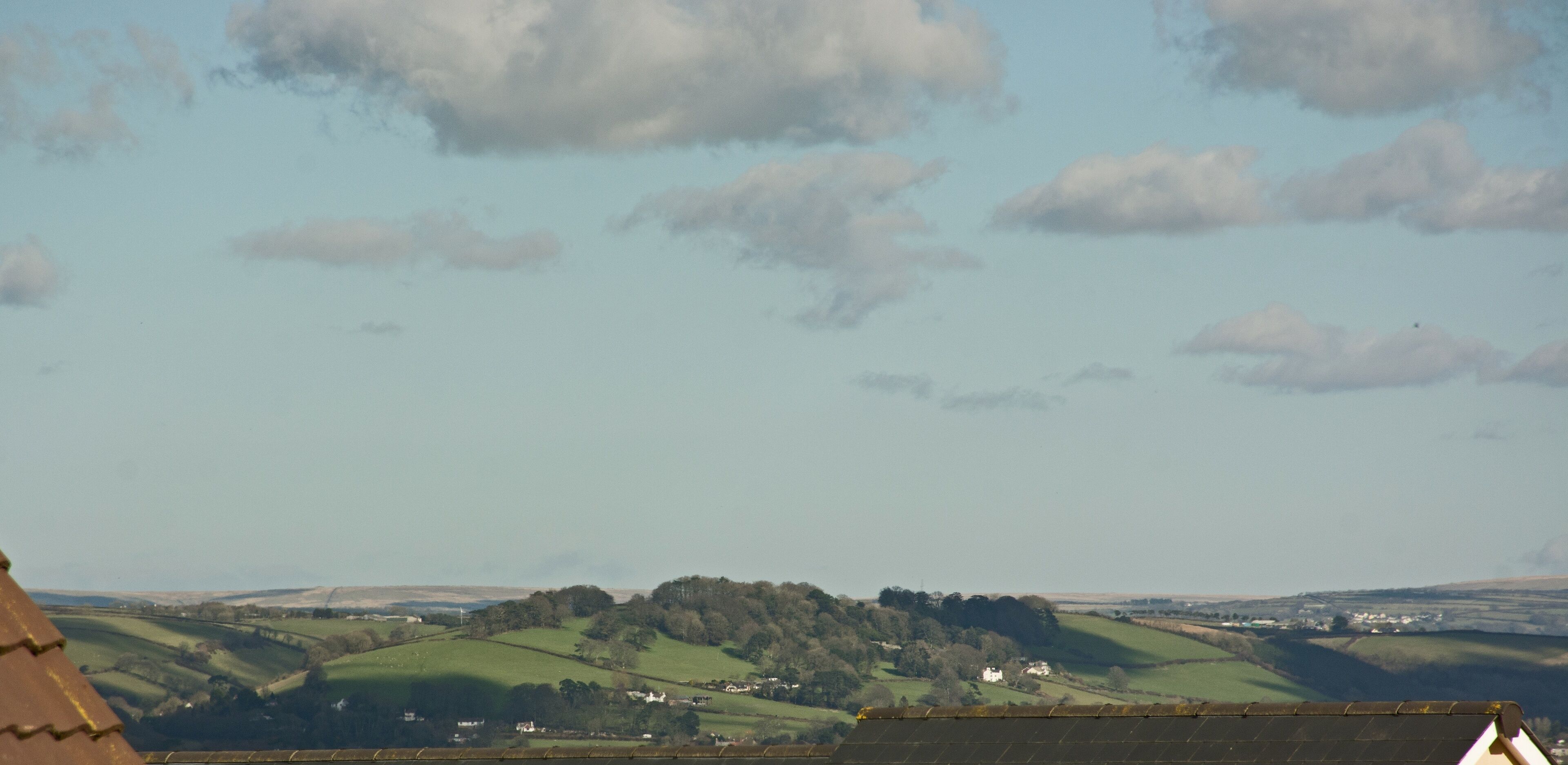 A rural landscape with rolling hills, scattered houses, and a clear sky with clouds.