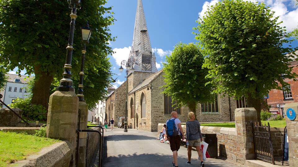 A church with a tall spire, a stone gate, and a street lined with trees.