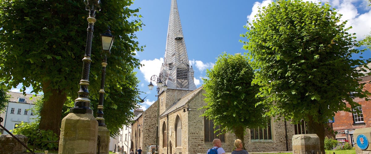 A church with a tall spire, a stone gate, and a street lined with trees.