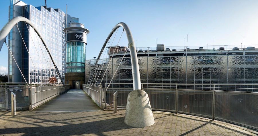 A pedestrian bridge with a glass facade and a metal arch structure.