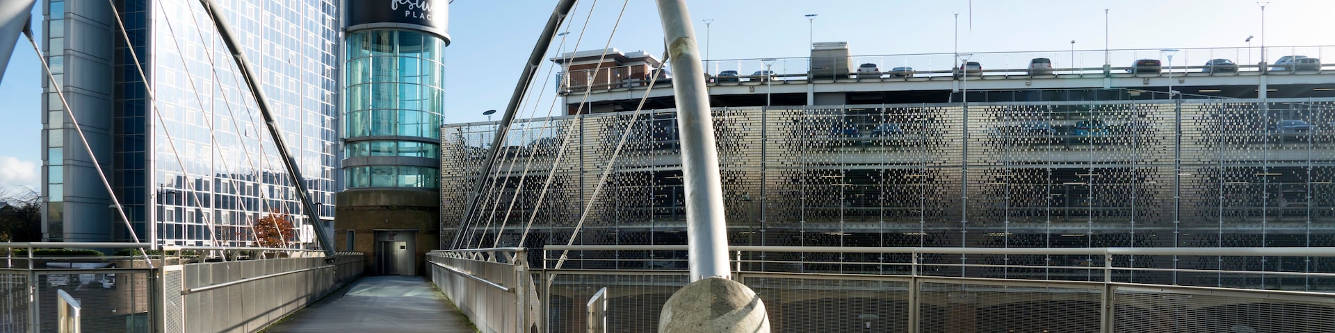 A pedestrian bridge with a glass facade and a metal arch structure.