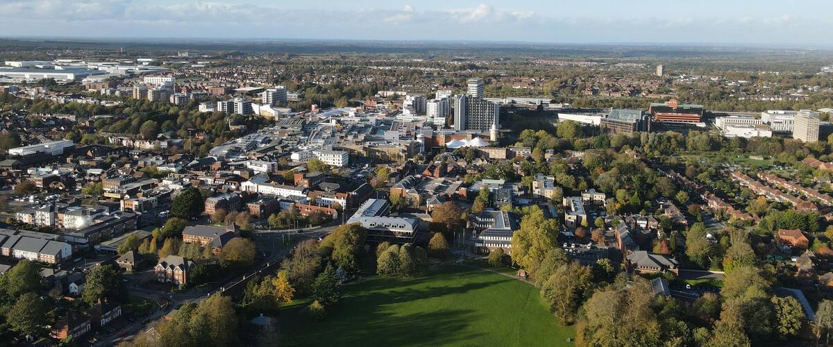 An aerial view of a city with dense urban development, green spaces, and a mix of residential and commercial buildings.