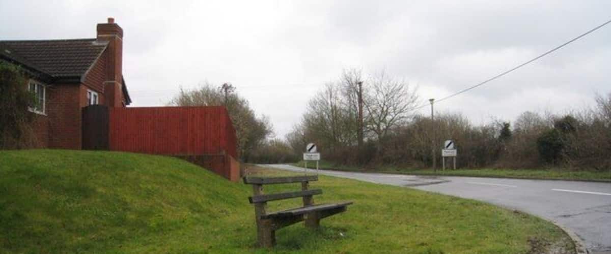 A rural road with a bench, a house, and a signpost.