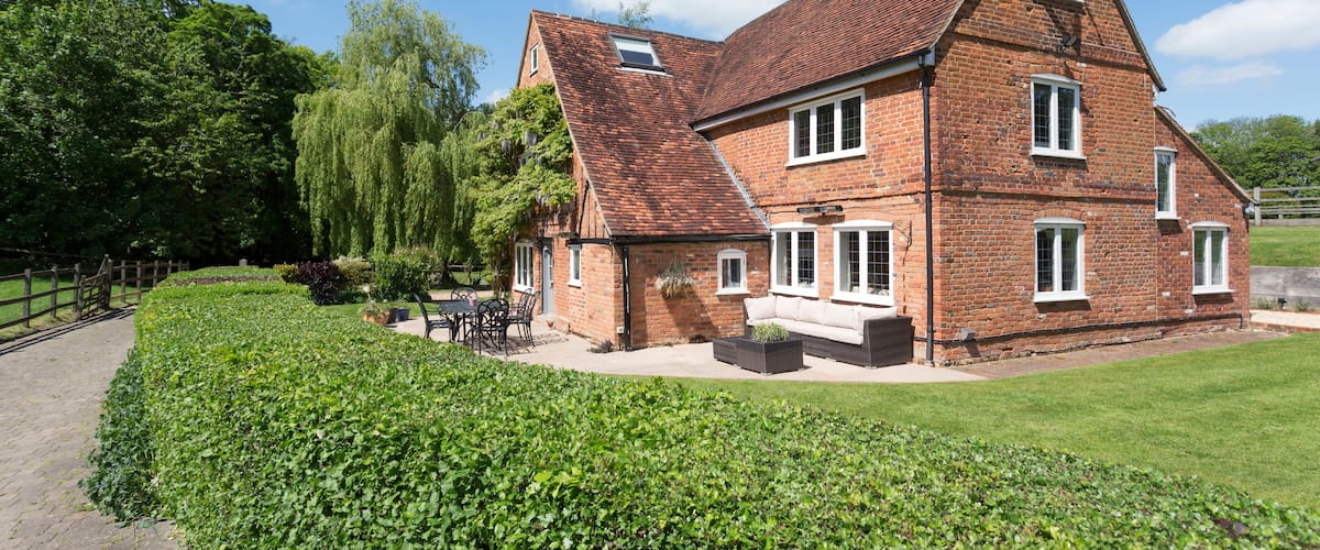 A large brick house with a sloped roof, surrounded by a well-maintained garden and a wooden fence.