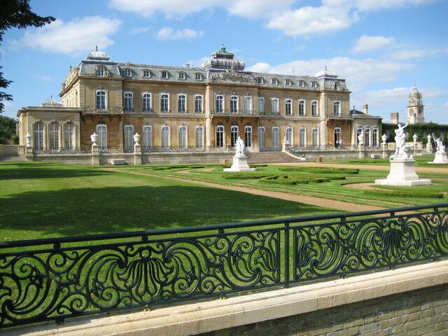 A large classical building with a symmetrical facade, a manicured lawn, and statues.