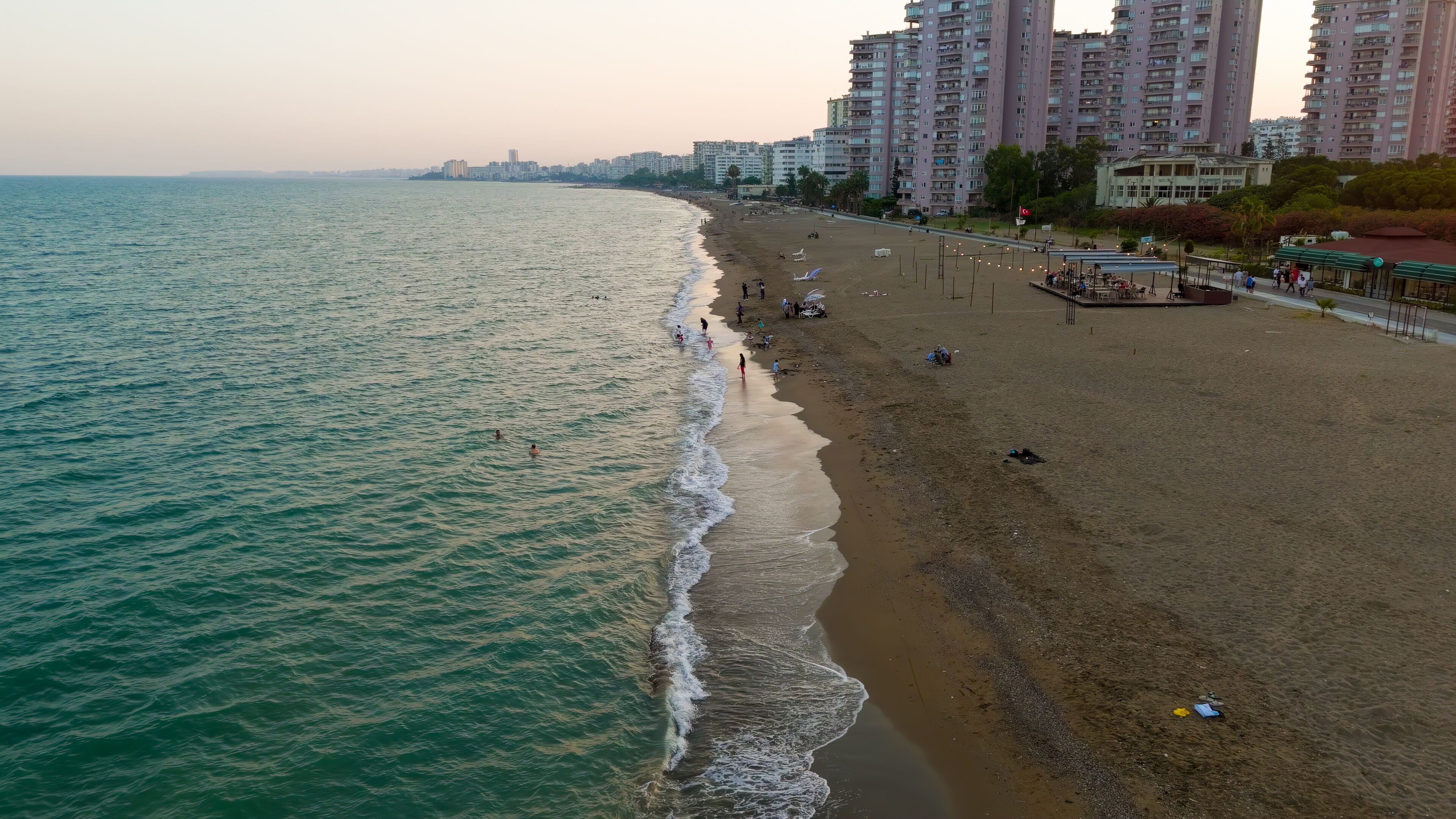 Mersin, Turkey. Low flight over wave surge line on beach with first line apartment buildings and relaxing people. Mezitli coastline.. Aerial View