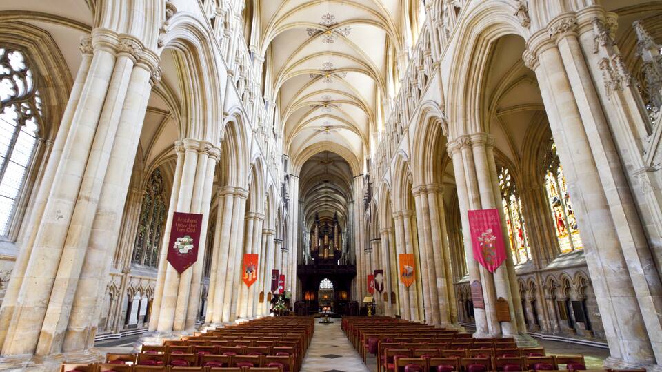 A cathedral interior with high vaulted ceilings, rows of wooden pews, and stained glass windows.