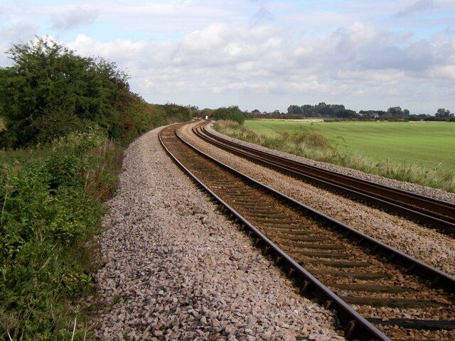 Railway tracks curving through a rural landscape with fields and trees.