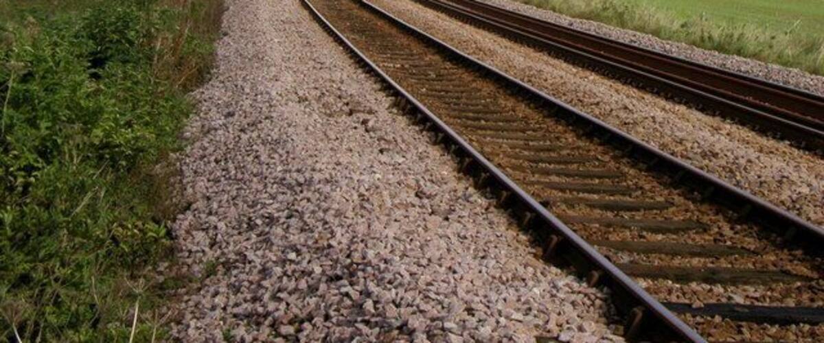 Railway tracks curving through a rural landscape with fields and trees.
