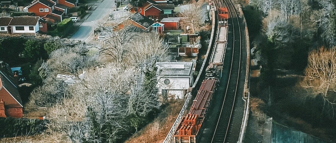 Trilhos de trem serpenteando por uma área residencial com casas e árvores.