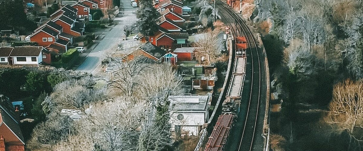 A railway track curving through a residential area with houses and trees.