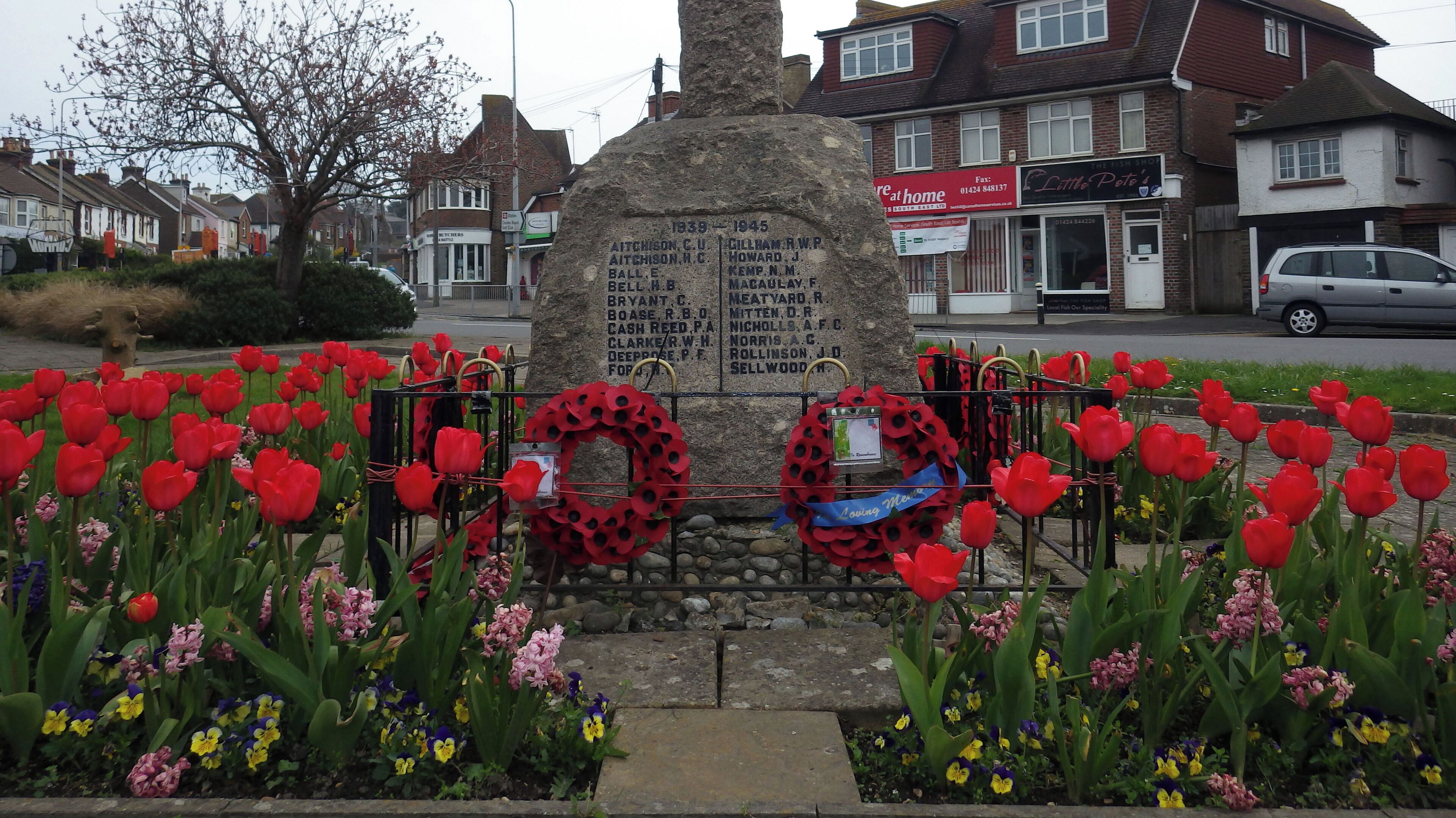 A memorial stone with names, surrounded by red tulips and poppy wreaths.