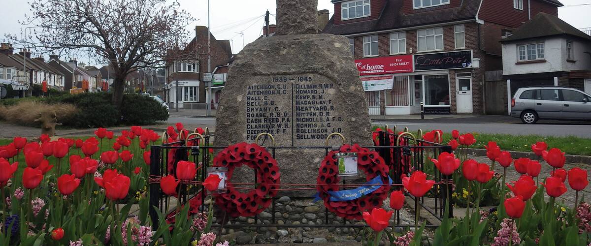 A memorial stone with names, surrounded by red tulips and poppy wreaths.