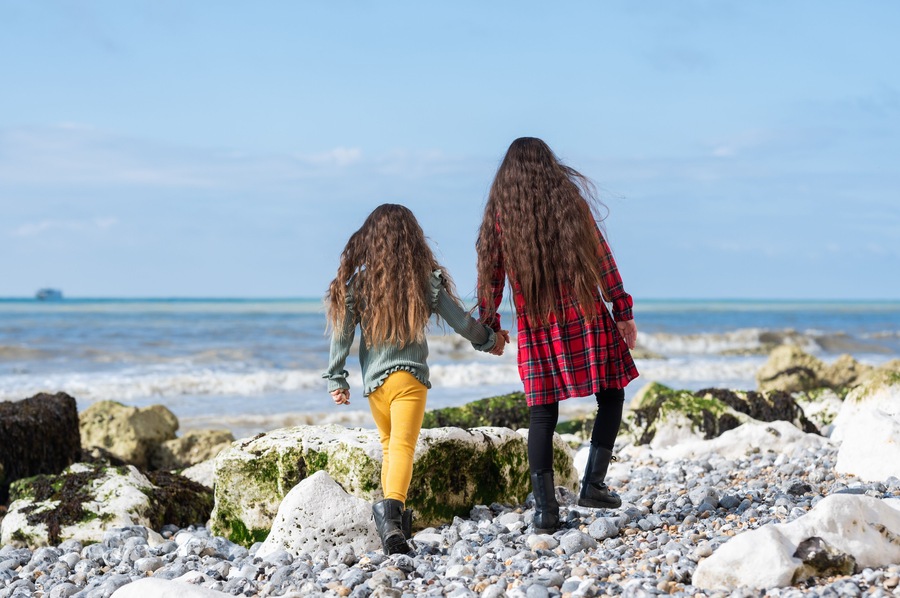 Two people walking on a rocky beach with the ocean in the background.