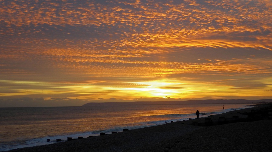 A sunset over a beach with waves and a person standing on the shore.