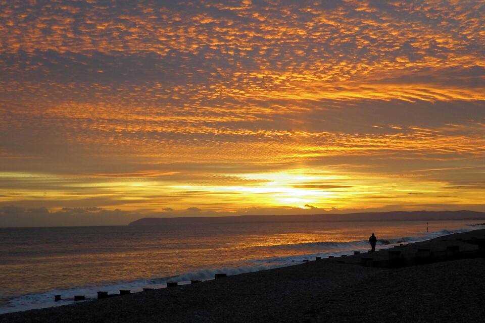 Un coucher de soleil sur une plage, avec des vagues et une personne debout sur le rivage.