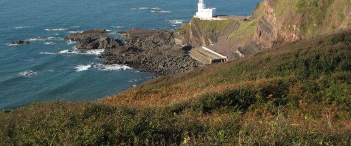 Un paisaje costero con un faro, acantilados rocosos y el océano.