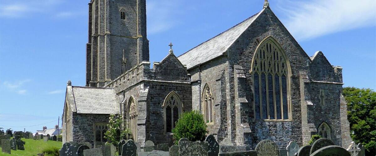 Una iglesia histórica con una alta torre y arquitectura gótica, rodeada por un cementerio.