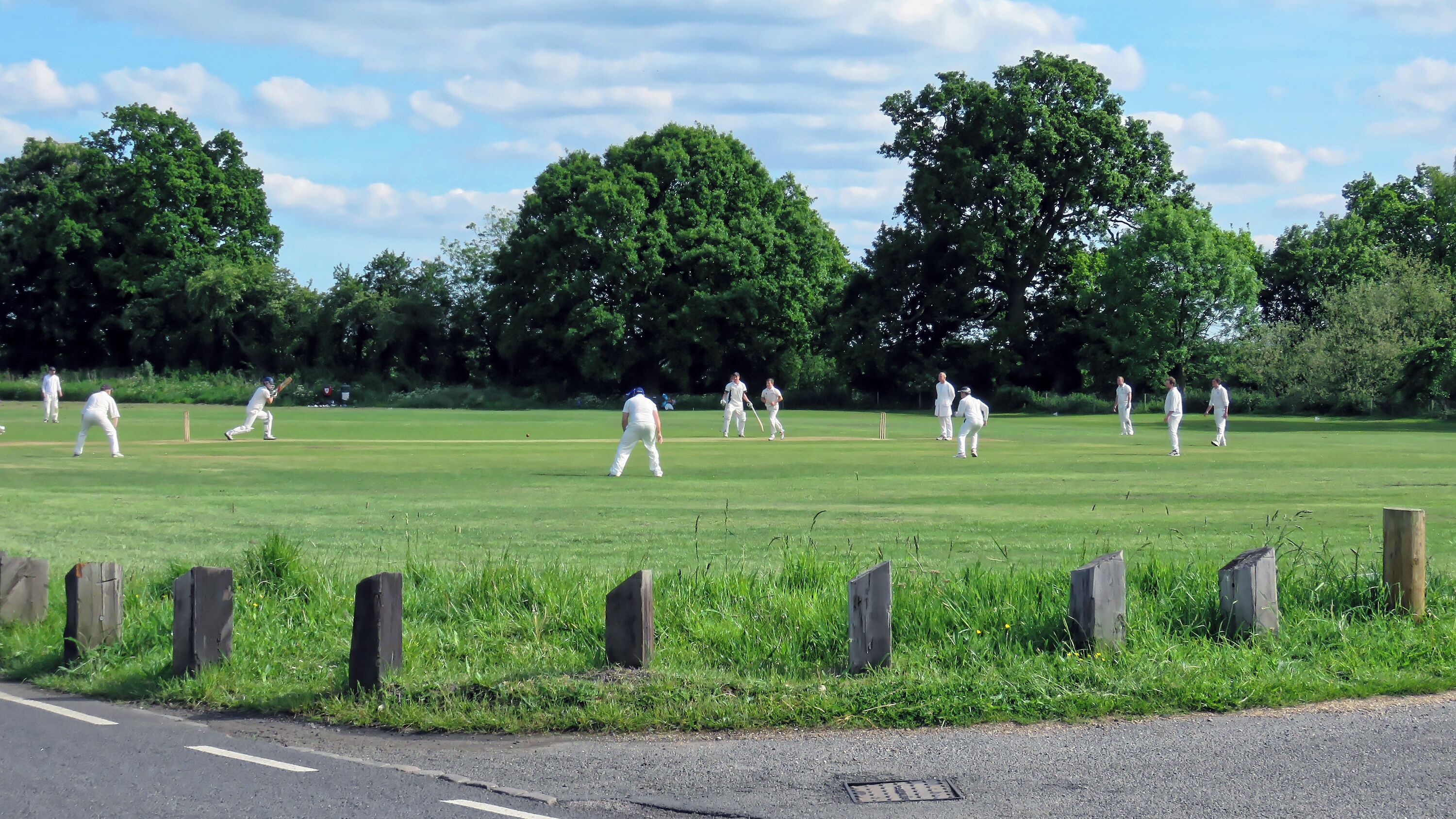 A Sunday cricket match between Hatfield Heath CC Friendly XI and Netteswell & Burnt Mill CC Sunday XI (Hatfield Heath batting), on the village green of Hatfield Heath, Essex, England. Hatfield Heath CC First XI play in the Herts and Essex Cricket League Division 2 (2017); Netteswell & Burnt Mill CC (The Millers), based at Harlow Cricket Club, is a social team for playing friendly matches. Camera: Canon PowerShot SX60 HS Software: File lens-corrected, optimized, perhaps cropped, with DxO OpticsPro 11 Elite, and likely further optimized with Adobe Photoshop CS2.