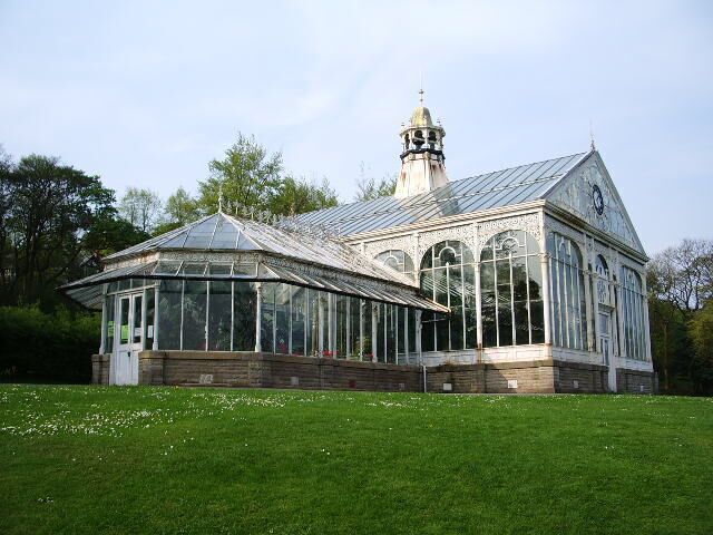 A large glass conservatory with a peaked roof, surrounded by a grassy area and trees.